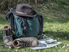 Wanderrucksack mit Hut und Wanderstiefel neben Wanderkarte und Kompass auf einer Wiese