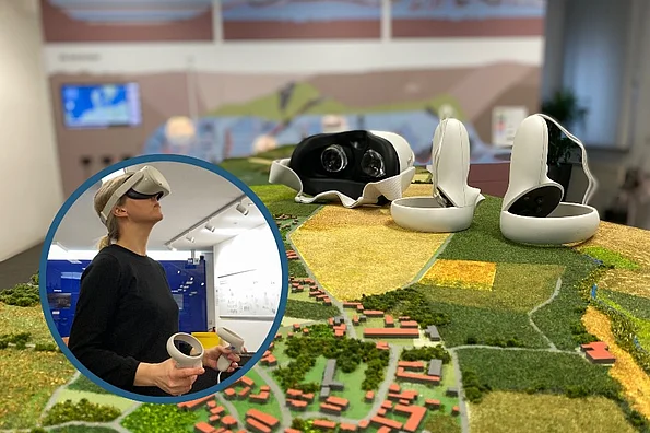 Foto von einer Modelllandschaft mit Feldern, Häusern und Straßen. Auf einem Hügel des Modells liegen eine weiße VR-Brille und zwei Controller.