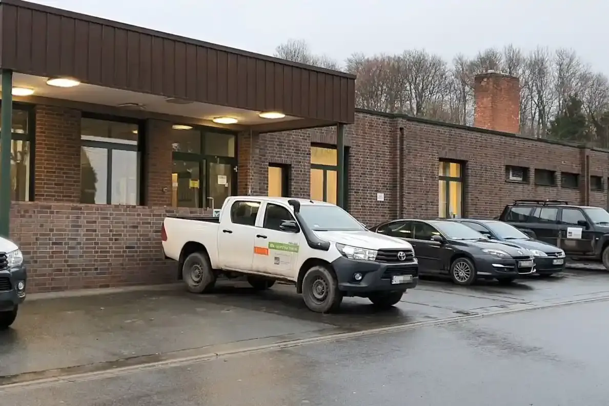 Ein Flachbau aus roten Backsteinen, vor dem mehrere Autos, unter anderem weiße Geländewagen, parken.