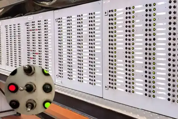 Das Hauptbild zeigt Eine graue Schalttafel mit Kippschaltern aus Metall und Glühlampen. Ein rundes Detailfoto zeigt drei Kippschalter und mehrere rote und grüne Lampen in der Nahaufnahme.