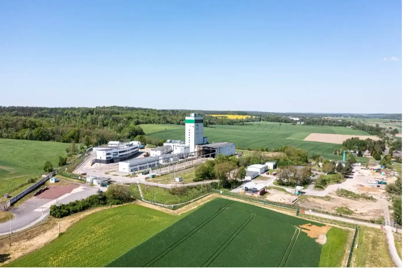 Die Luftaufnahme des Endlagers Morsleben zeigt einen Industriekomplex mit weißen Gebäuden in einer Landschaft mit grünen Feldern und einem blauen Himmel.