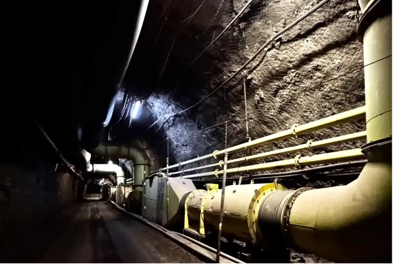 Foto eines Tunnels in einem Bergwerk. Am rechten Rand verlaufen mehrere Rohre und Kabel. 