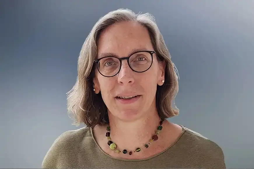 Eine Frau mit einem blonden Bob-Haarschnitt und einer schwarzen Brille blickt freundlich in die Kamera.