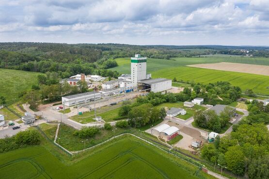 Luftansicht auf eine Industrieanlage inmitten von Feldern und Bäumen. Im Zentrum der Anlage steht ein weißer Turm.
