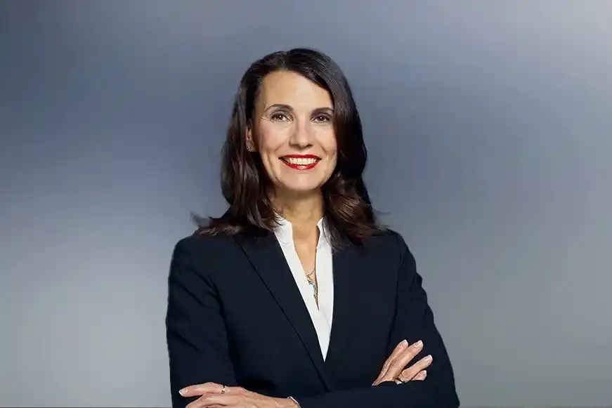 Porträtfoto einer Frau mit schulterlangen dunkelbraunen Haaren. Sie trägt einen schwarzen Blazer und darunter eine weiße Bluse. 