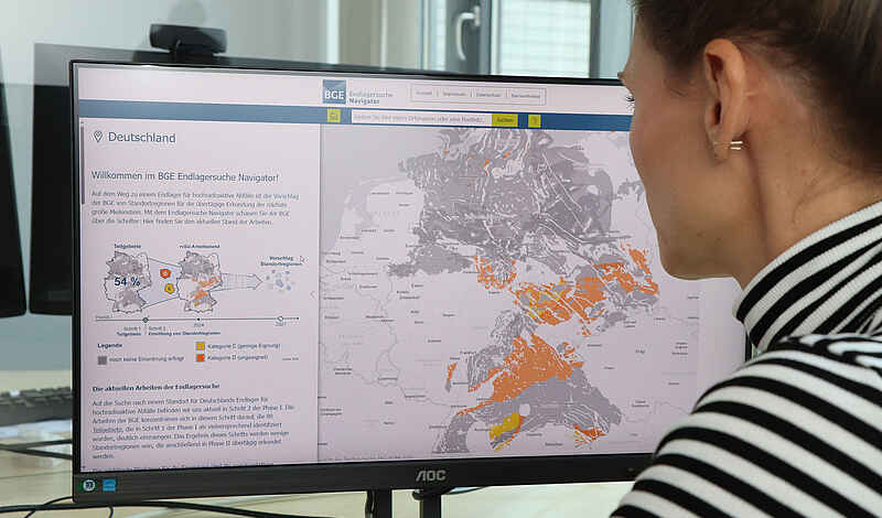 Foto einer Frau, die vor einem Computerbildschirm sitzt. Der Computerbildschirm zeigt eine Kartenanwendung.