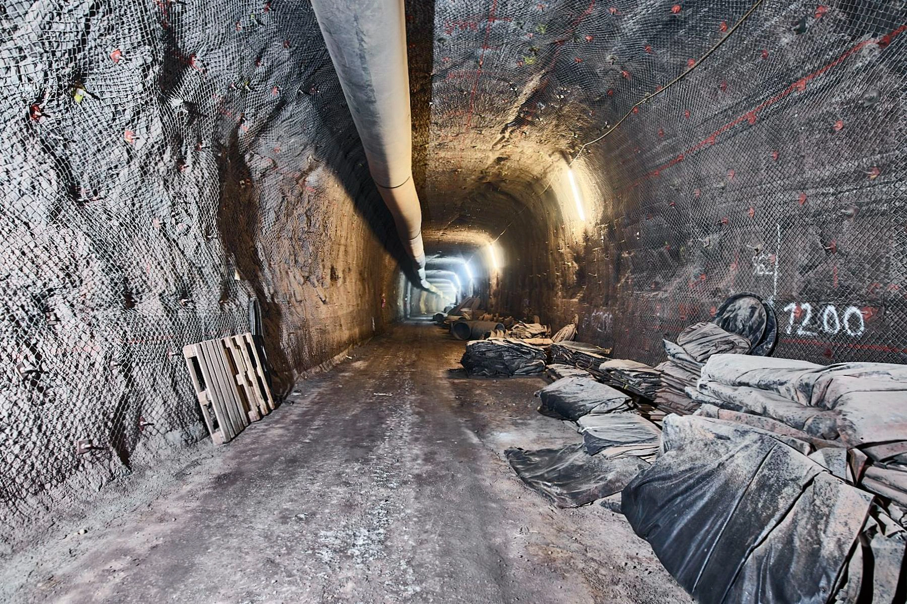 A long underground tunnel with a large pipe running along the ceiling.