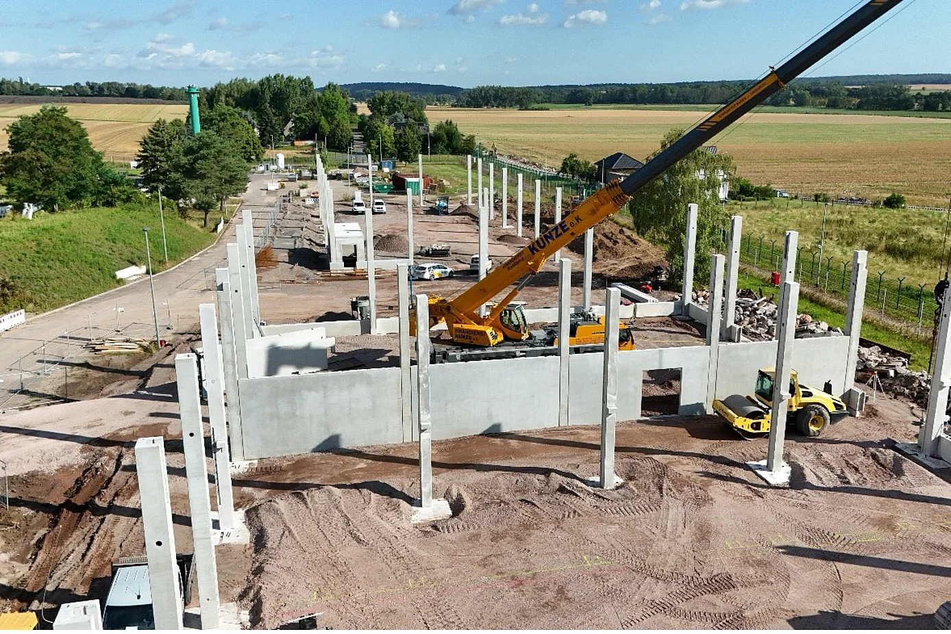 Das Bild zeigt eine Baustelle mit 49 aufgestellten Stützen und einem Kran, der Betonfertigteile platziert.