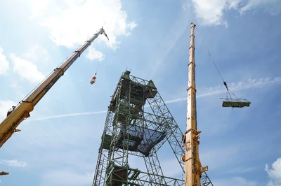 Blick auf das provisorische Fördergerüst. Zu sehen sind zwei Autokräne, die für die Demontage benötigt werden. An einem hängen die Fachkräfte, die den Turm demontieren, an dem anderen wird gerade ein großes Stahlteil zum Erdboden befördert.
