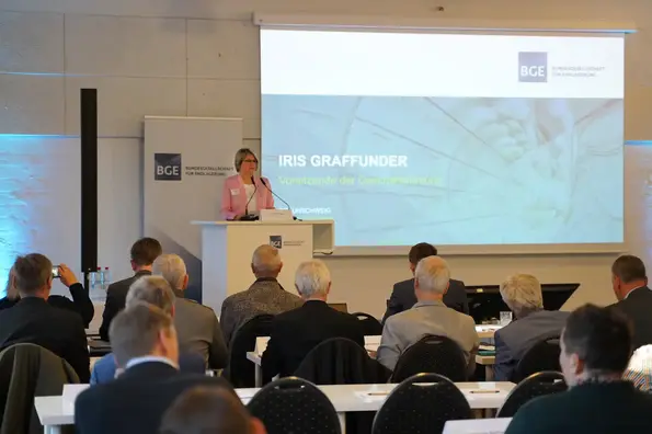 Ein Publikum bei einer Informationsveranstaltung, eine weibliche Person trägt etwas vor.