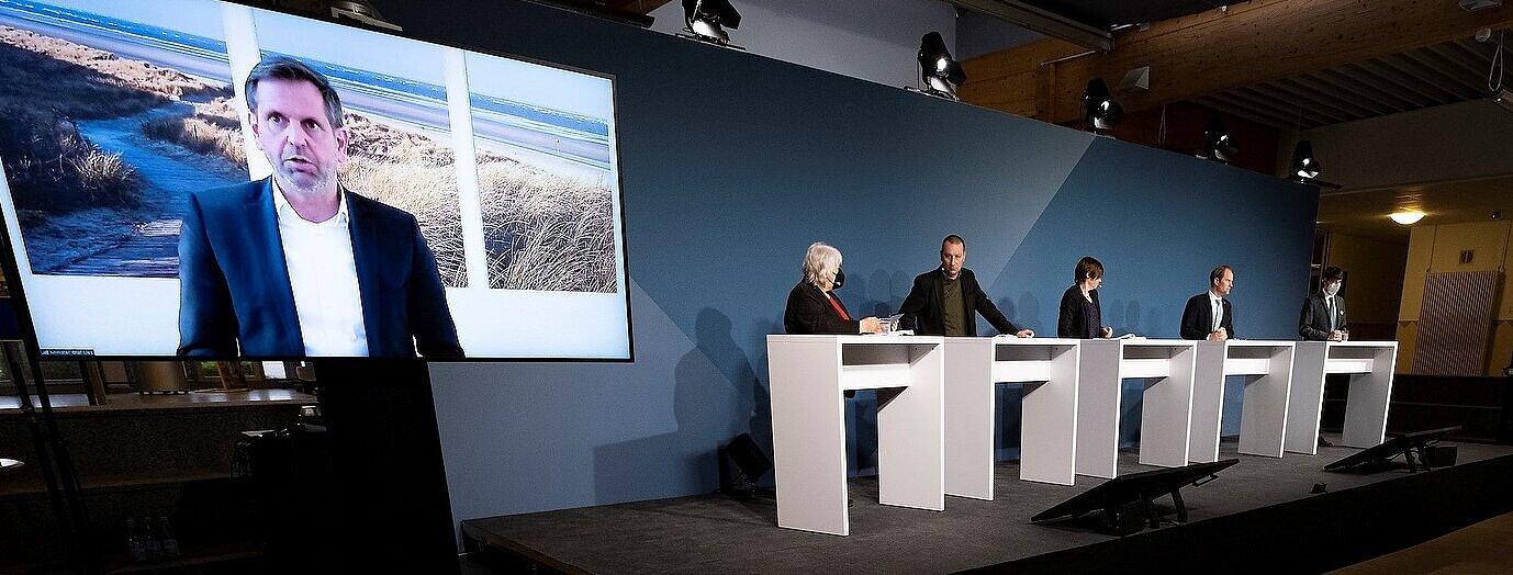 Vier Personen stehen an Pulten auf einem Podium.