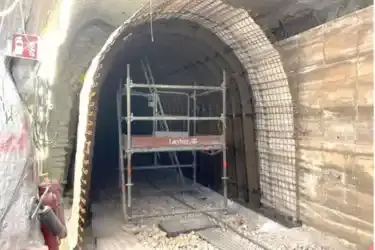 Foto einer halbrunden Gitterstruktur in einem Bergwerk unter Tage. Hinter der Gitterstruktur befinden sich gebogene Metallträger. Gemeinsam erzeugt die Konstruktion den Eindruck eines Tunnels unter Tage.