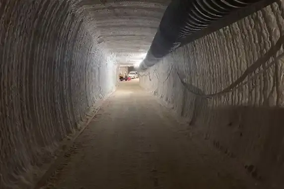 Alternativtext: Foto eines Tunnels in einem Salzbergwerk unter Tage. An der Decke und der rechten Wand verlaufen Kabel und Rohre.