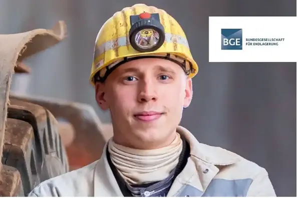 Portrait-Foto eines Mannes mit gelbem Schutzhelm mit Helmlampe. Er trägt weiße Bergmannskleidung und ein weißes Halstuch.  