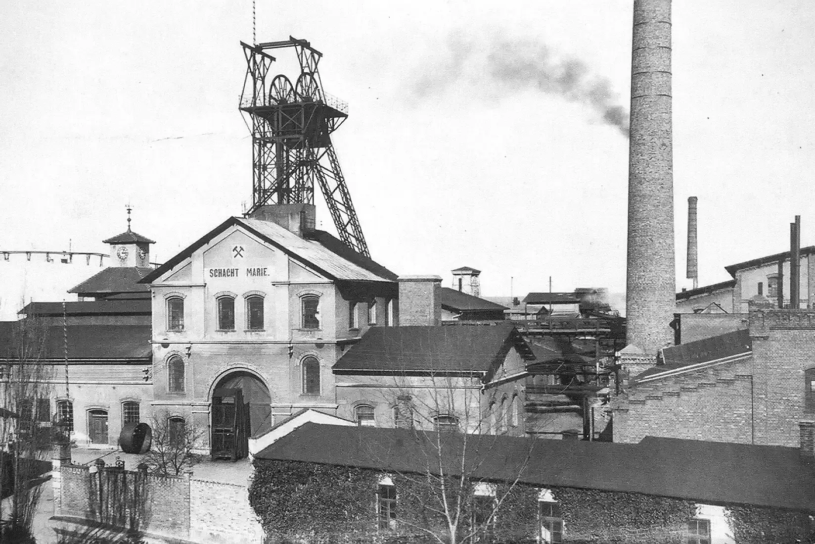 Black and white photo from 1922 showing several large buildings, the factory chimney and the headframe of Marie shaft.