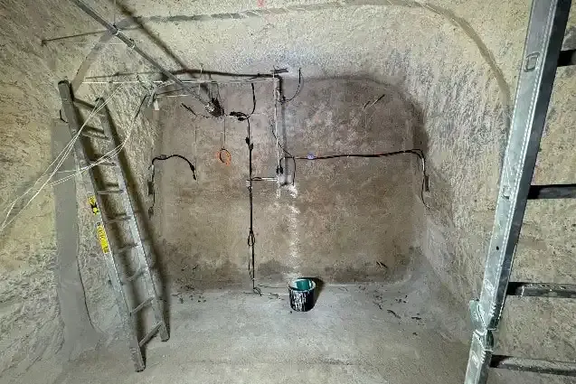Foto eines verfüllten Tunnels unter Tage in einem Salzbergwerk. An der verfüllten Wand befinden sich Messgeräte, seitlich davon stehen Leitern.