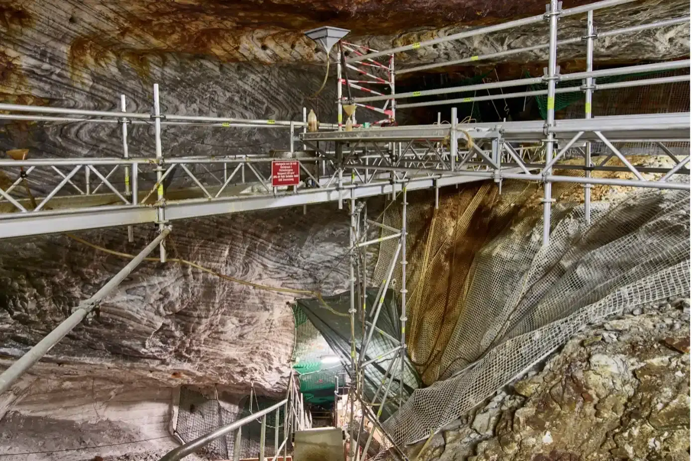 In einer steilen Abbaukammer unter Tage befinden sich ein Gerüst, Eimer, Absperrvorrichtungen und Netze. 