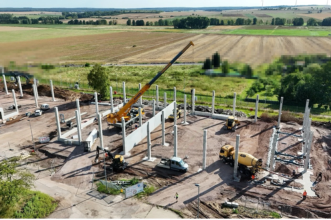 Das Bild zeigt eine Baustelle mit 49 aufgestellten Stützen und einem Kran, der Betonfertigteile platziert.