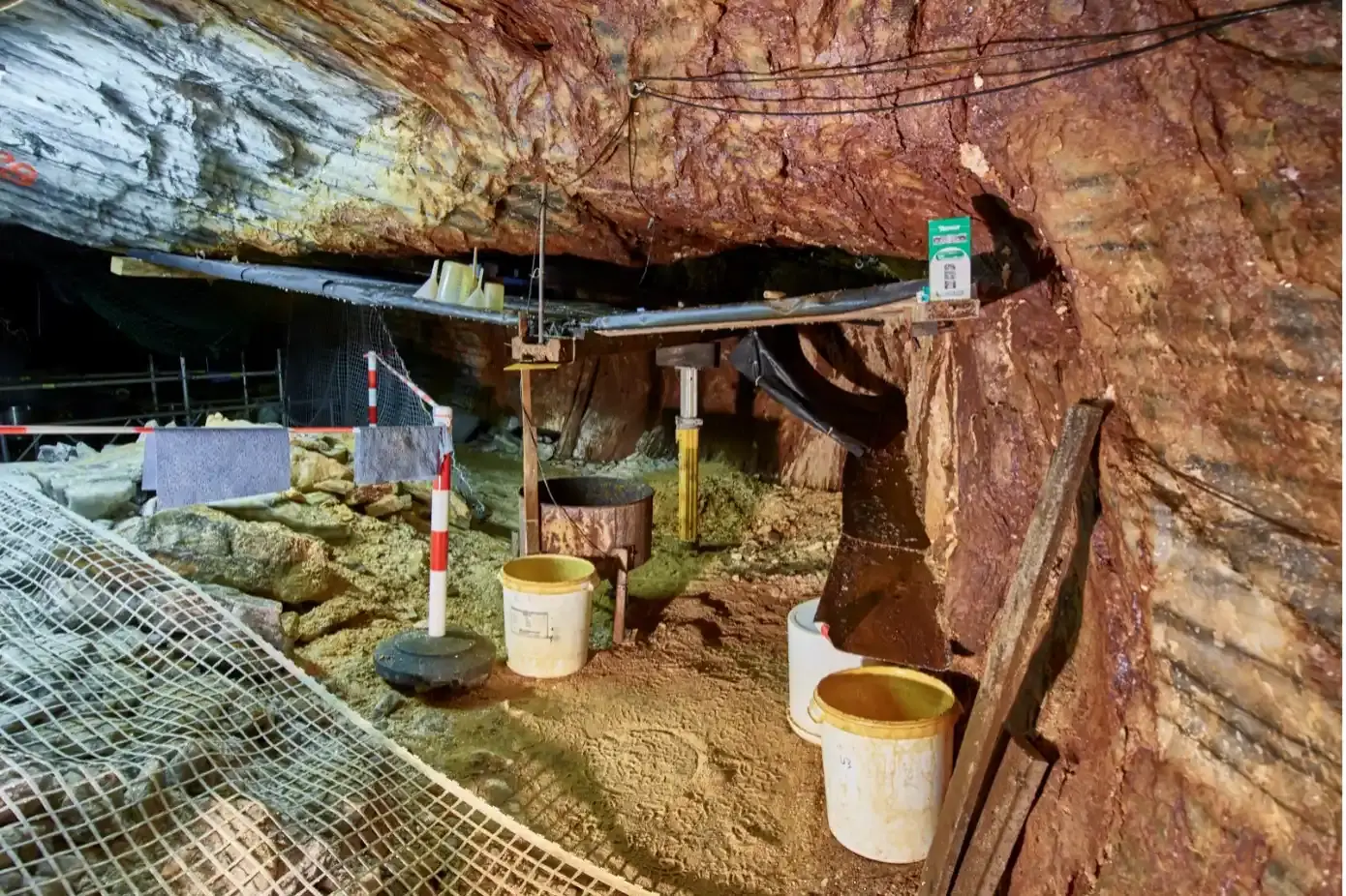 In einer steilen Abbaukammer unter Tage befinden sich ein Gerüst, Eimer, Absperrvorrichtungen und Netze. 