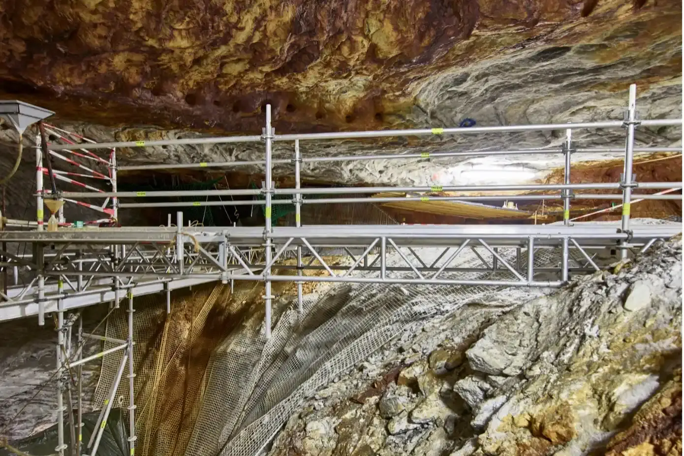 In einer steilen Abbaukammer unter Tage befinden sich ein Gerüst, Eimer, Absperrvorrichtungen und Netze.