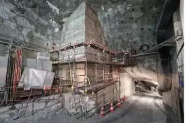 Foto einer Baustelle unter Tage in einem Salzbergwerk. In der Mitte des Bildes befindet sich eine große gemauerte Konstruktion, die von der Form her an einen Kamin erinnert. Um die Konstruktion herum befindet sich ein Gerüst. Pylonen sichern die Baustelle am Fuß der Konstruktion ab.