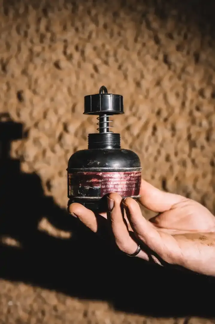 Eine Hand hält ein schwarzes Messgerät aus Kunststoff mit rotem Aufkleber. Das Messgerät ist am unteren Ende bauchig und mündet nach einem schmalen Hals in einem Deckel mit kleiner Öse.