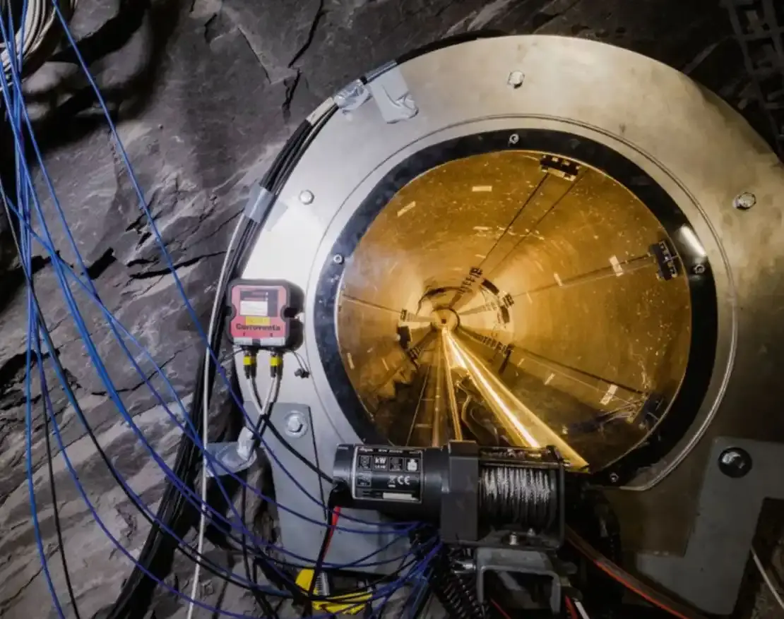 Das Foto zeigt einen langen, gelb erleuchteten Tunnel in einem Fels. Der Tunnel ist mit einer dicken Glasscheibe verschlossen und zahlreiche Messgeräte sind dort installiert.