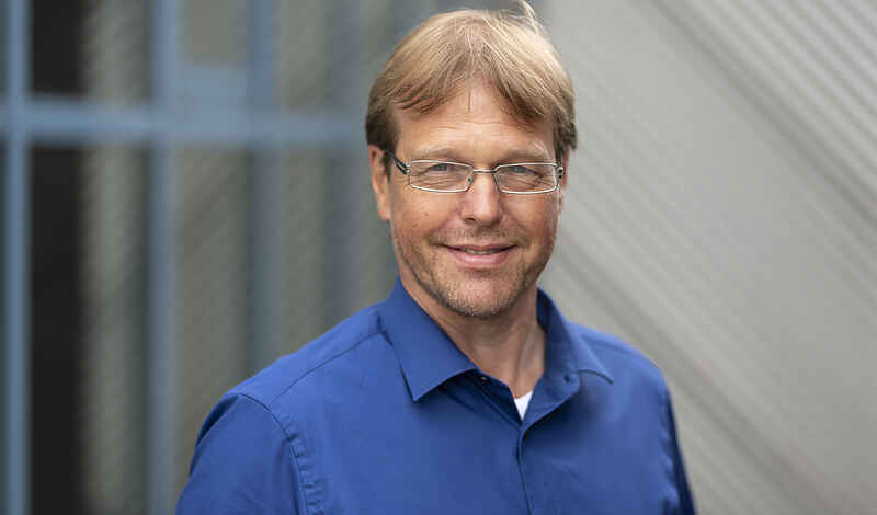 Portraitfoto von einem Mann mit Brille, dunkelblondem Haar und blauem Hemd.