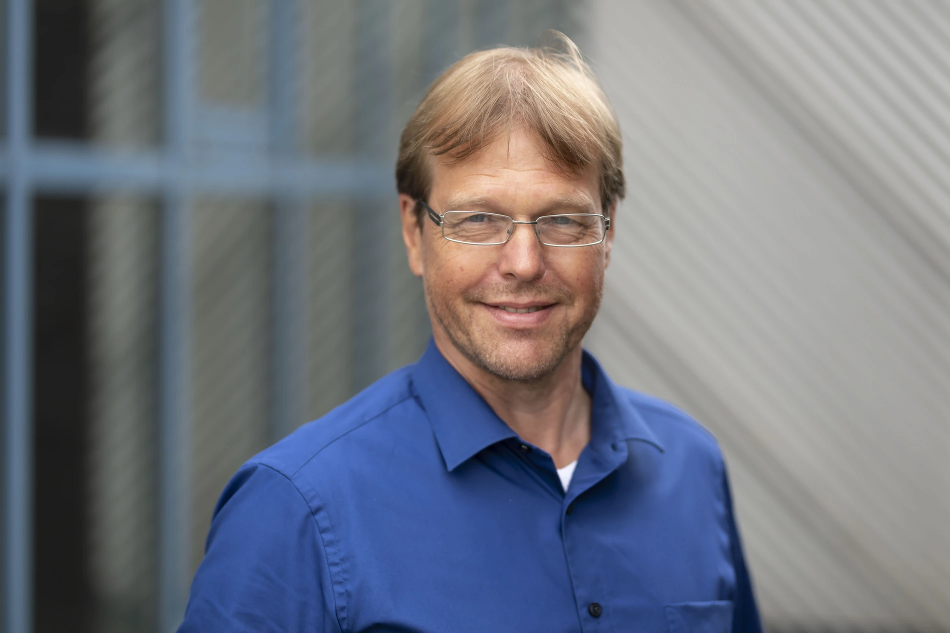 Portraitfoto von einem Mann mit Brille, dunkelblondem Haar und blauem Hemd.