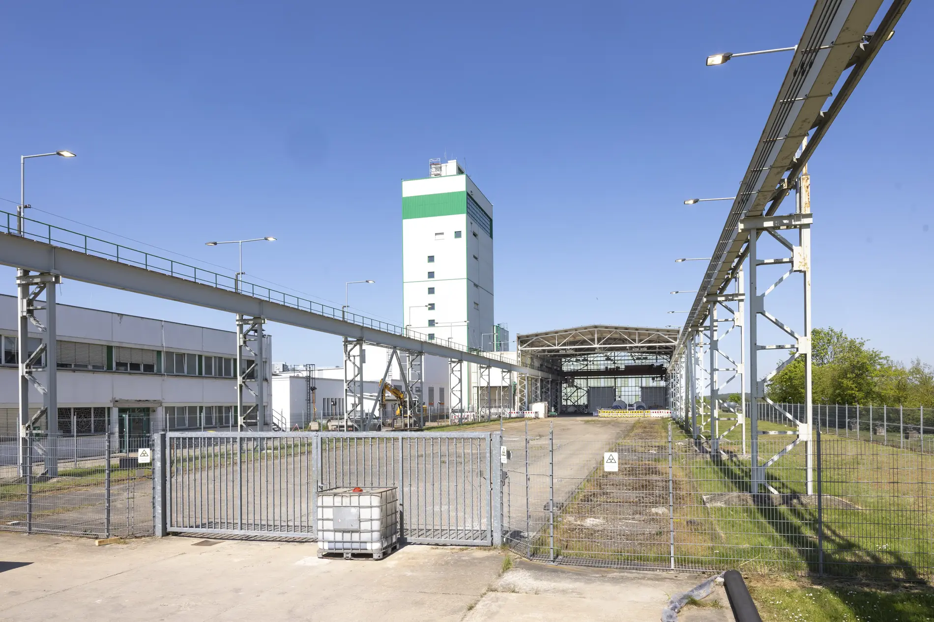 The site of the Morsleben repository is set against a blue sky behind a large gate. The white winding tower rises into the air. 