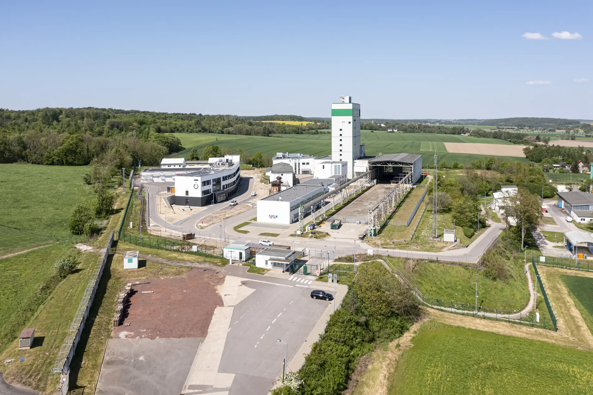 The Morsleben repository photographed from the air. The site, including the white winding tower, is surrounded by green fields and forests under a blue sky.