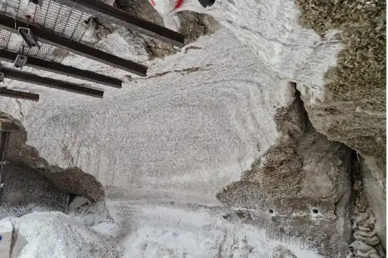 Das Bild zeigt eine Wand aus Steinsalz. Der mittlere Teil der Wand weist Spuren einer Fräse auf und erscheint deutlich heller als der umgebende Bereich. Am Boden davor liegt loses, weißes Salz auf einem Haufen. Unter der Decke sind mehrere Stahlträger eingezogen. Auf der rechten Seite der Wand klafft ein Riss vertikal durch die Wand.