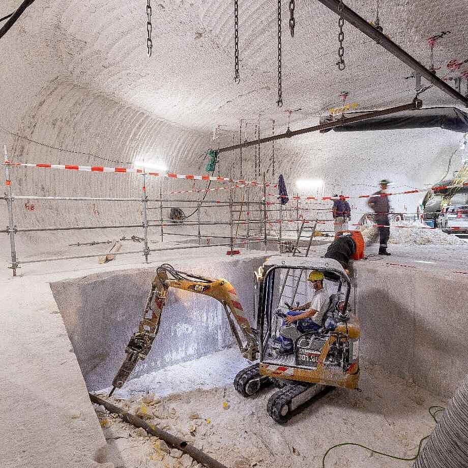 Ein Bagger und Bergleute in einem Bohrkeller unter Tage.