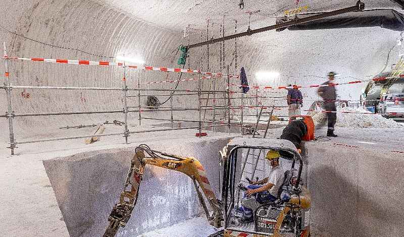 Ein Bagger und Bergleute in einem Bohrkeller unter Tage.