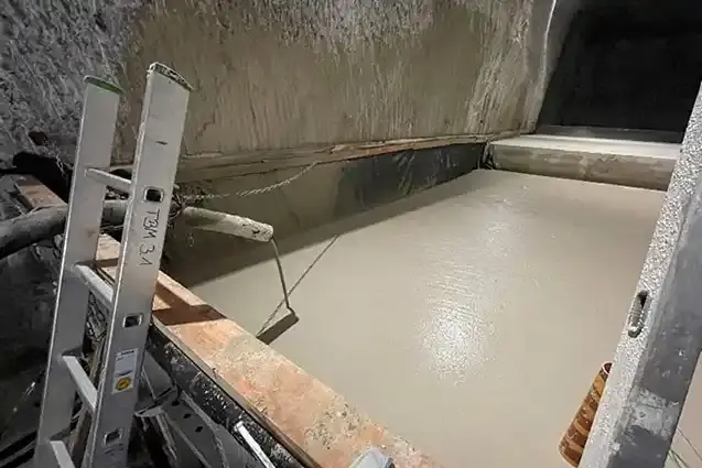 Foto eines gemauerten Beckens unter Tage, in dem gräulicher flüssiger Beton lagert.