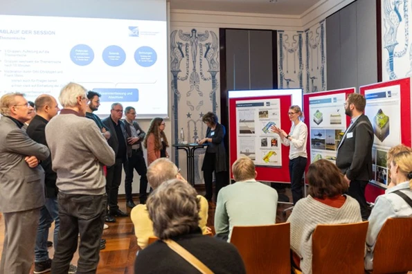 Viele Leute stehen vor Postern an Stellwänden, vor denen Mitarbeiter*innen der BGE Fragen beantworten. 