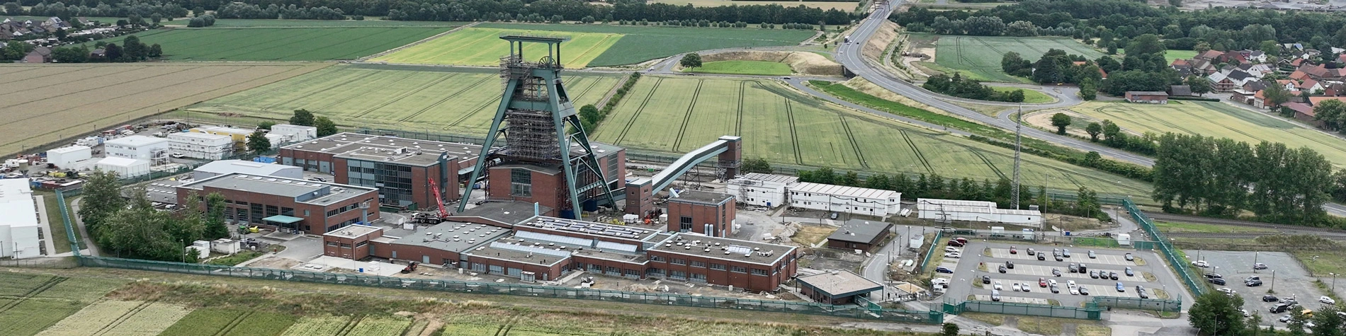 Die Luftaufnahme des Endlagers Konrad zeigt mehrere Industriegebäude und einen Förderturm. Die Anlage wird von Feldern und Straßen umringt.