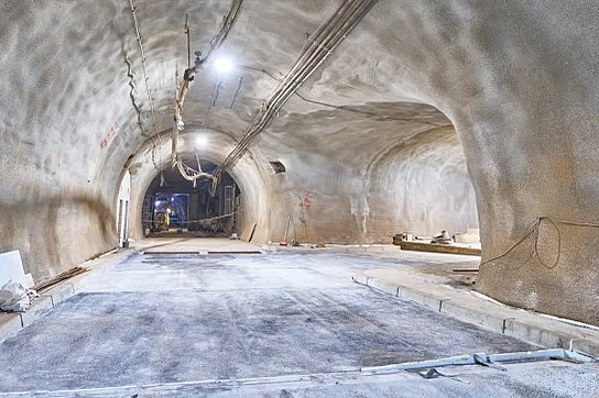 Blick in einen hell erleuchteten Tunnel in einem Bergwerk. An der Decke verlaufen Kabelstränge. Der Boden wurde zu einer Fahrbahn ausgebaut. An deren Seiten befinden sich Begrenzungssteine, die an einen Bürgersteig erinnern.