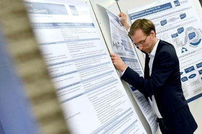 Ein Mann befestigt ein Plakat mit wissenschaftlichen Texten und Grafiken an einer Wand.