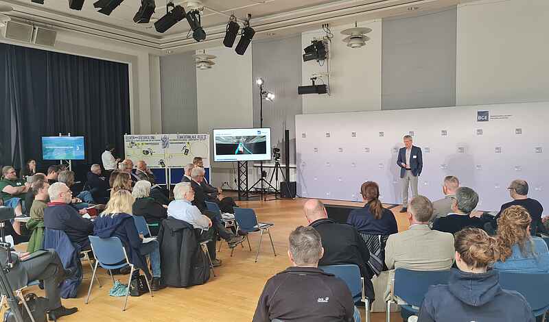 Das Bild zeigt einen Blick in die Eulenspiegelhalle. Dort steht eine Person und spricht. Die Gäste der Veranstaltung sitzen auf Stühlen.