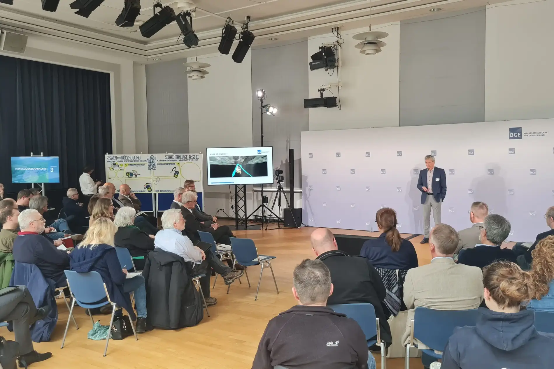 Das Bild zeigt einen Blick in die Eulenspiegelhalle. Dort steht eine Person und spricht. Die Gäste der Veranstaltung sitzen auf Stühlen.