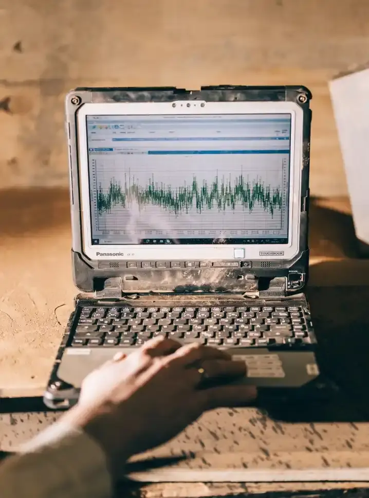 Ein Notebook zeigt im Bildschirm Messergebnisse in einem Diagramm an. Eine Hand bedient das Touchpad.