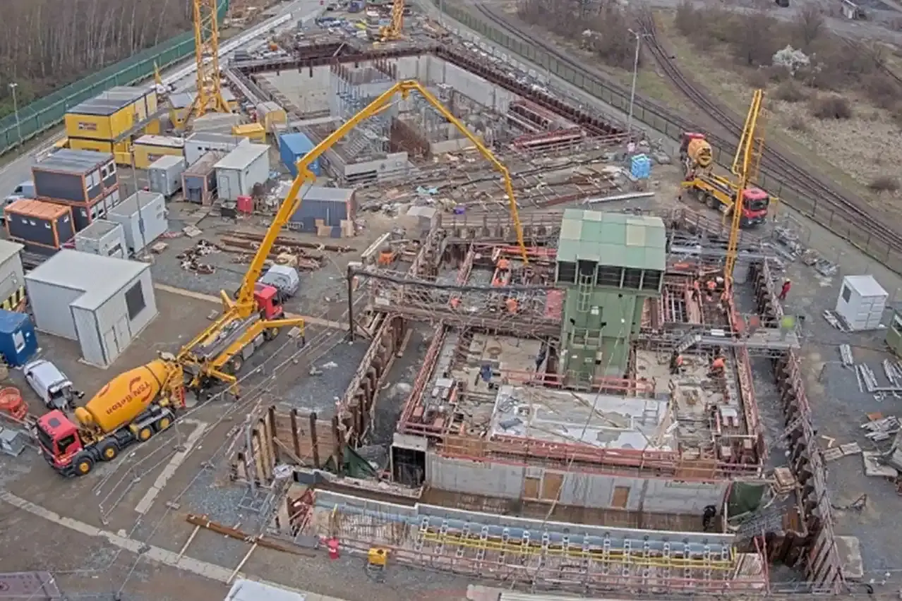 Aus der Vogelperspektive ist eine Baustelle zu sehen. Ein Betonmischer und eine Betonpumpe werden für die Betonage neben einem grünen Haus eingesetzt.