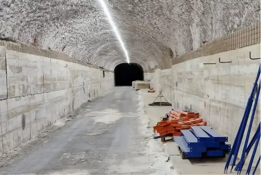 Das Bild zeigt den Blick in eine Strecke im Bergwerk. Über die ersten Meter erstrecken sich graue Betonwände an beiden Seiten der Strecke. Quer auf den Betonwänden sind mehrere Stahlträger verbaut, die die Wände verbinden. Im hinteren Teil schließt sich ein Bereich an, in dem die Strecke durch mehrere, hintereinander verbaute, halbrunde Stahlbögen gestützt wird.