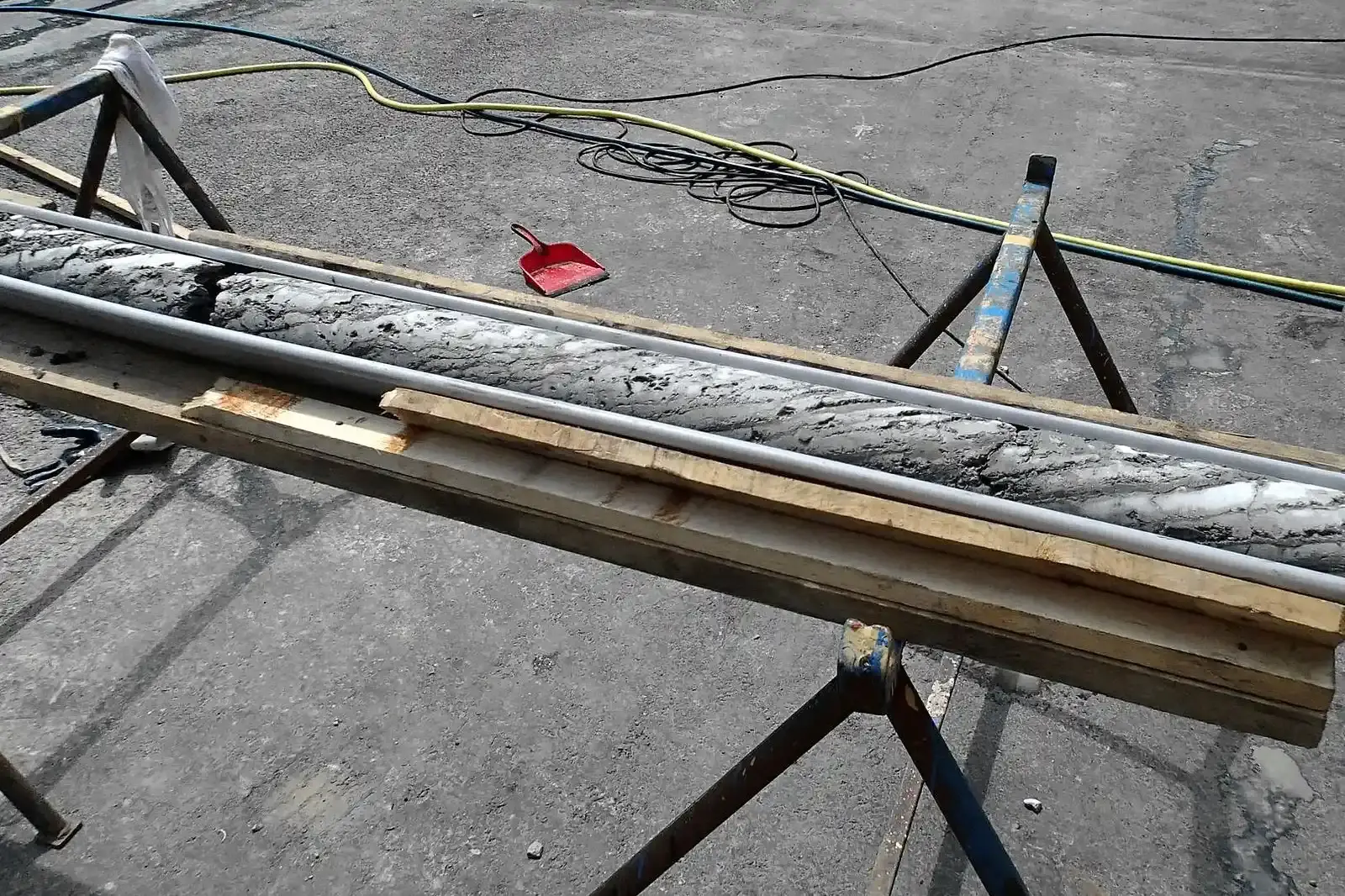 Ein zylindrischer Gesteinskörper liegt in einer Metallrinne auf zwei Böcken.