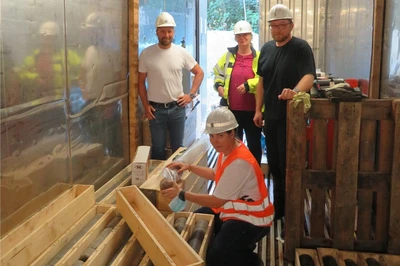 In einem Container lagern auf dem Boden Holzkisten mit den 1 Meter langen Bohrkernen. Sebastian Kunze (Fa. Angers), Dr. Silke Marczinek (BGE), Stephan Pfeiffer (Ercosplan) und Christiane Tänzer (BGE) sichten den letzten Bohrkern der Erkundungsbohrung R11.