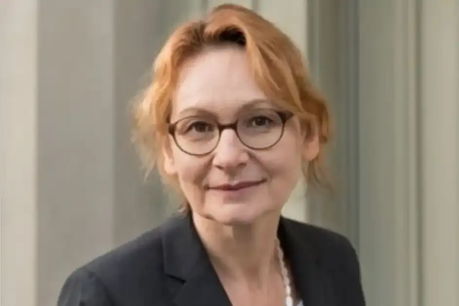Portraitfoto einer Frau im schwarzen Blazer, Brille und roten Haaren.