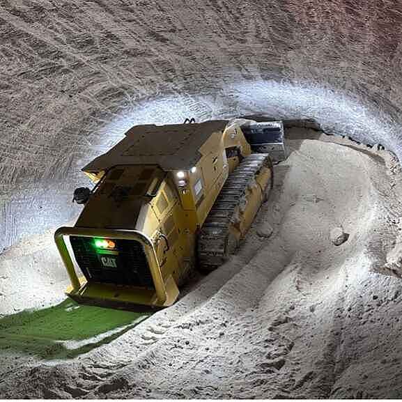 Eine gelbe Kettenraupe schiebt loses Salz in einen Tunnel eines Salzbergwerks und türmt das Salz am Ende des Tunnels auf.