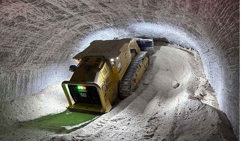 Eine gelbe Kettenraupe schiebt loses Salz in einen Tunnel eines Salzbergwerks und türmt das Salz am Ende des Tunnels auf.