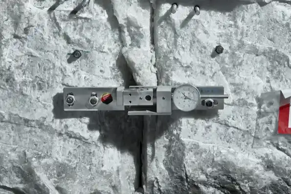 Das Bild zeigt die Nahaufnahme eines grauen Salzgesteins. Das Gestein weißt einen Riss auf. Ein Messgerät aus Metall ist an der Wand befestigt.